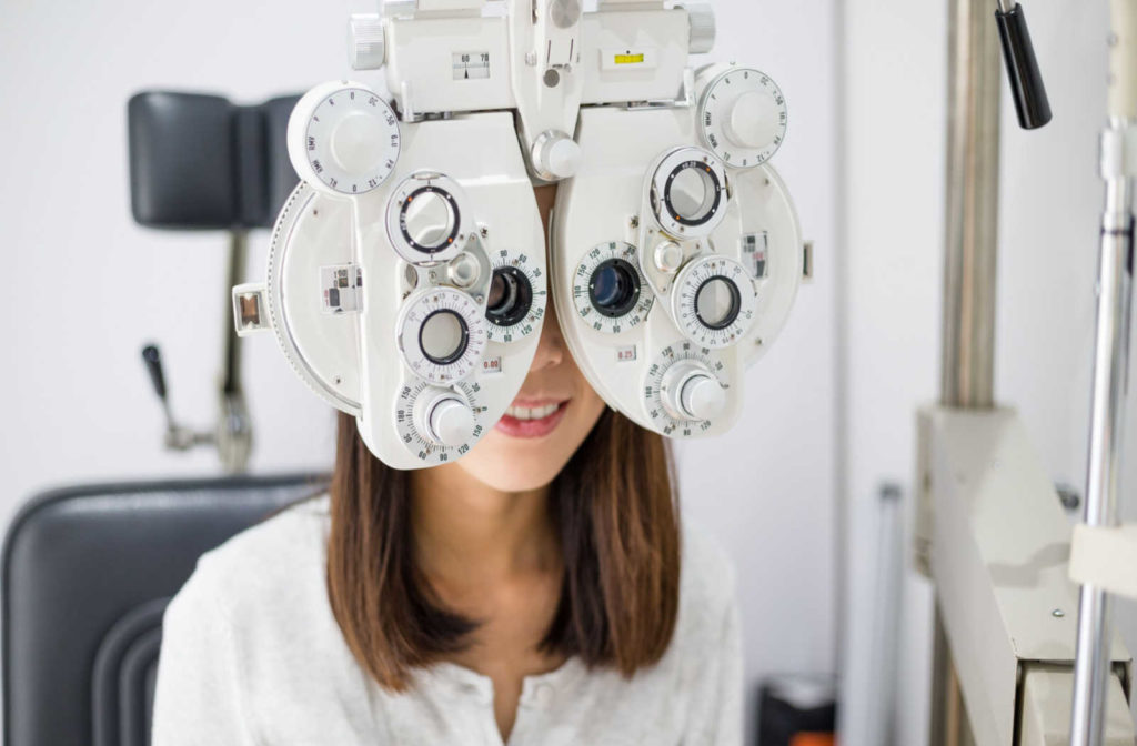 A young woman gets her visual acuity assessed while looking through a phoropter.