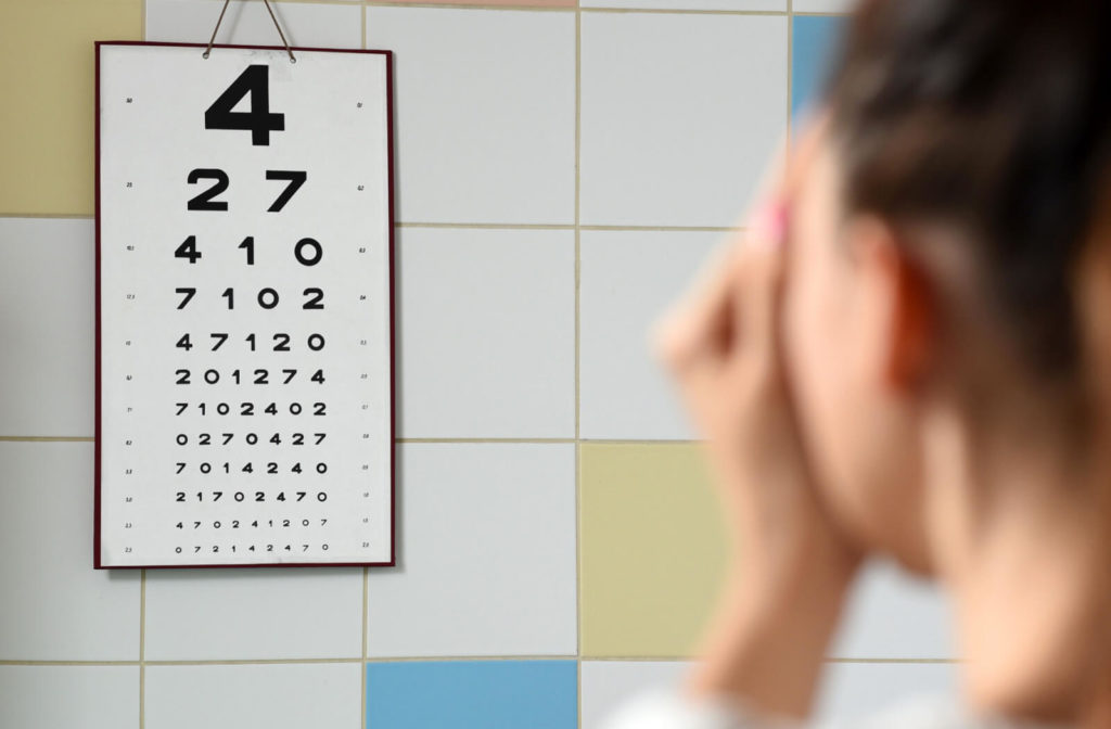 A woman is looking at an eye test chart at far while covering her left eye with her left hand.