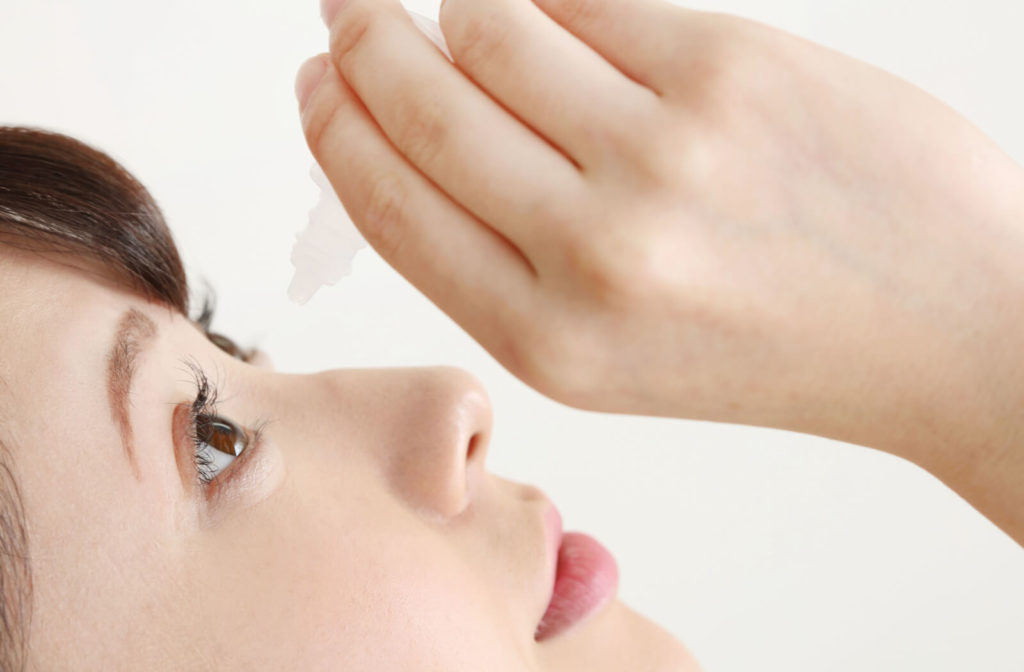A young woman is pouring some drops of rewetting eye drops on her eyes to keep her eyes well lubricated