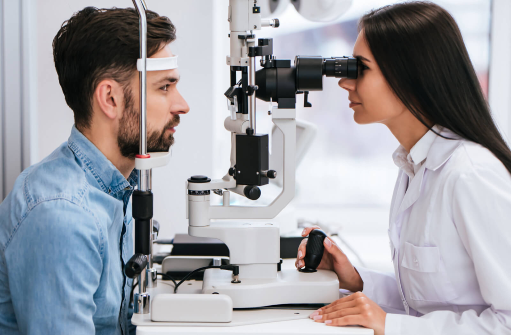 A female optometrist examining the eyes of a young man using a medical device to detect potential eye problems.
