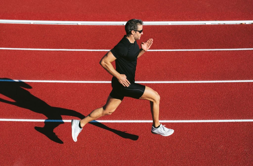 A man wearing sunglasses and fitness clothes running on a track.