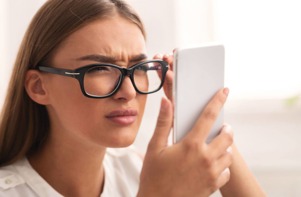 A woman with eyeglasses, squinting to see clearly on her smartphone.
