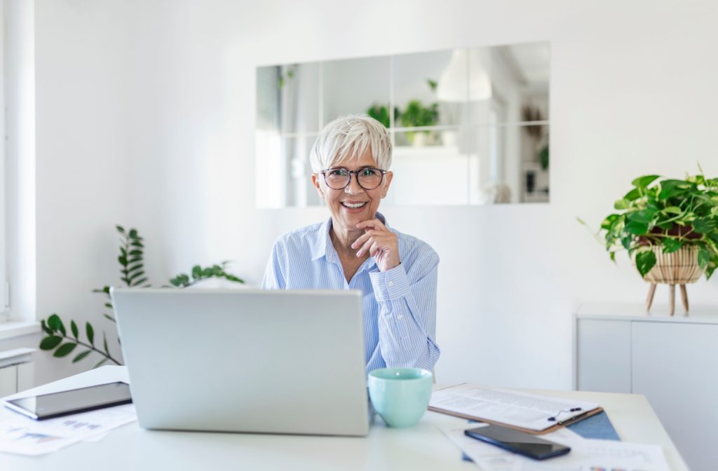 A mature woman helps prevent the onset of CVS by practicing good posture, wearing blue light glasses, and working in a well-lit environment.