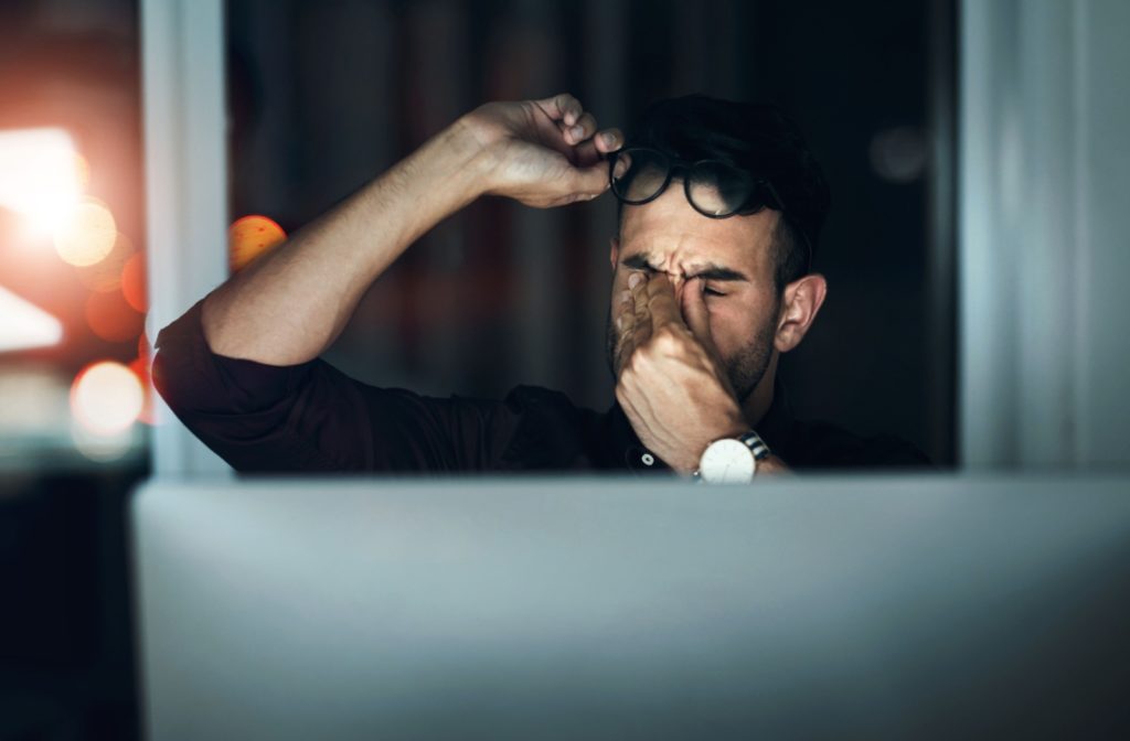 A young man rubs his eyes after experiencing fatigue from prolonged computer work.