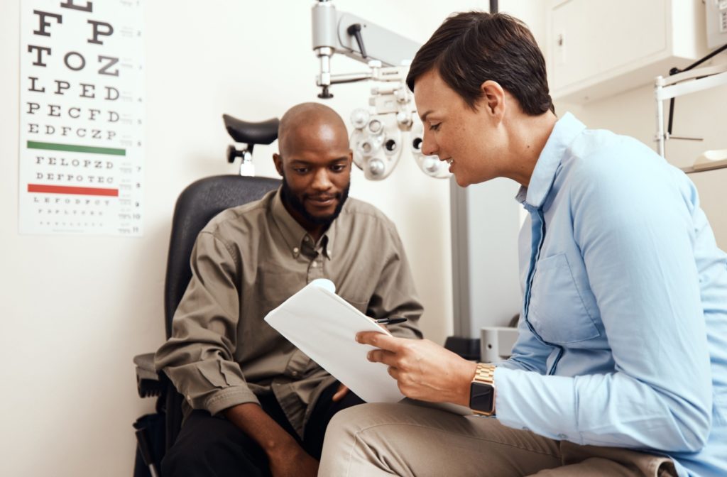 An optometrist in her office explaining to a patient how he can prevent styes in the future.