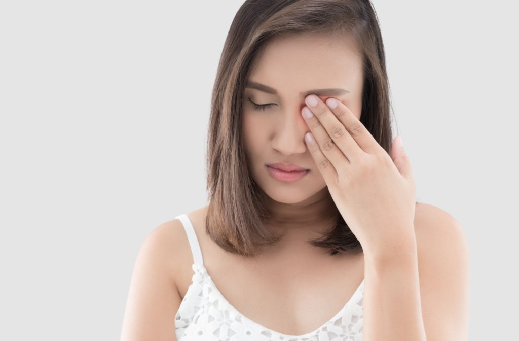 A woman rubbing her left eye in frustration due to a recurring stye.