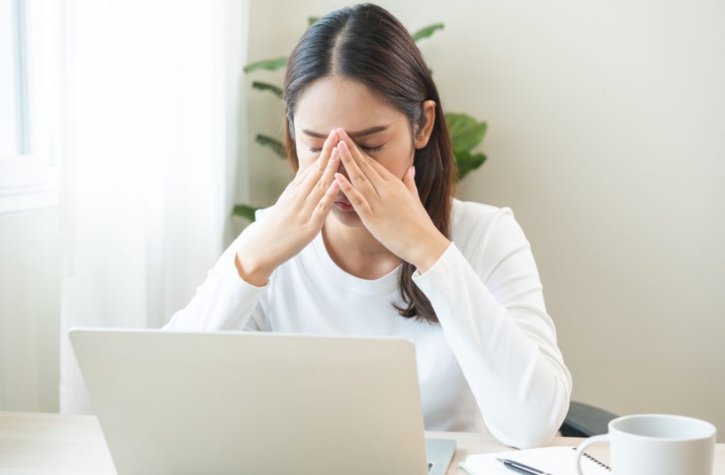 A tired young woman working at her laptop, rubbing her eyes in frustration because she's blinking too much.