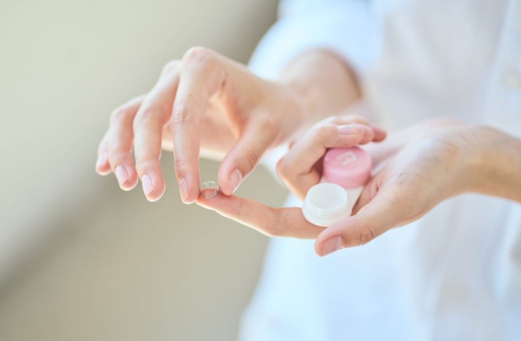 An individual holds a contact lens container in one hand while balancing a contact lens on their finger as they prepare to pick it up.