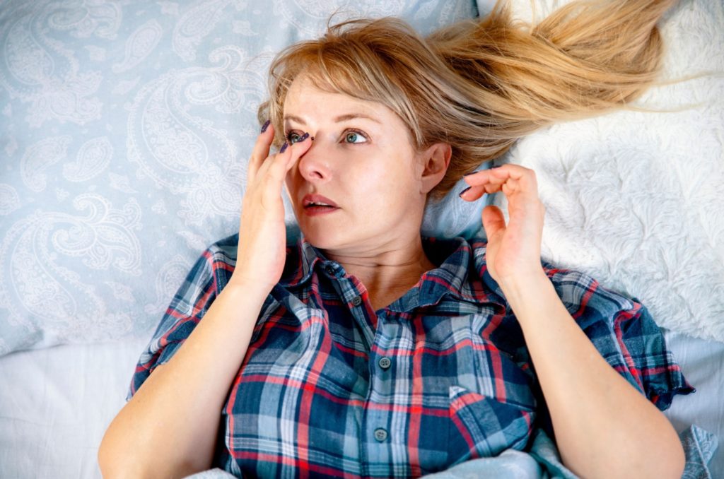 A woman rubbing their sore right eye while lying in bed.