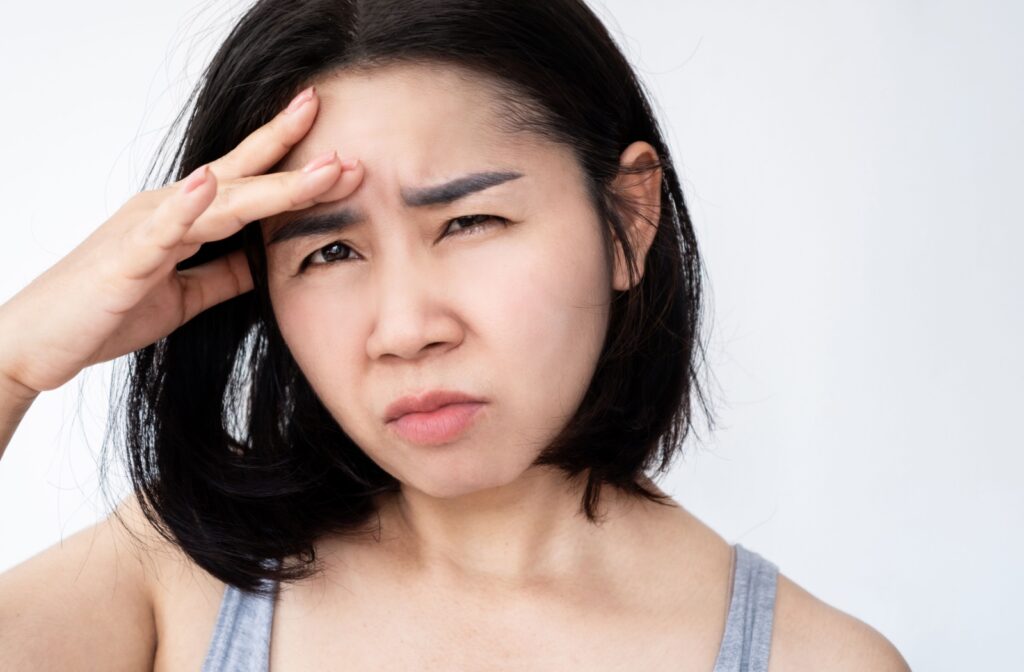 A person puts their hand to their forehead and squints uncomfortably from light sensitivity.