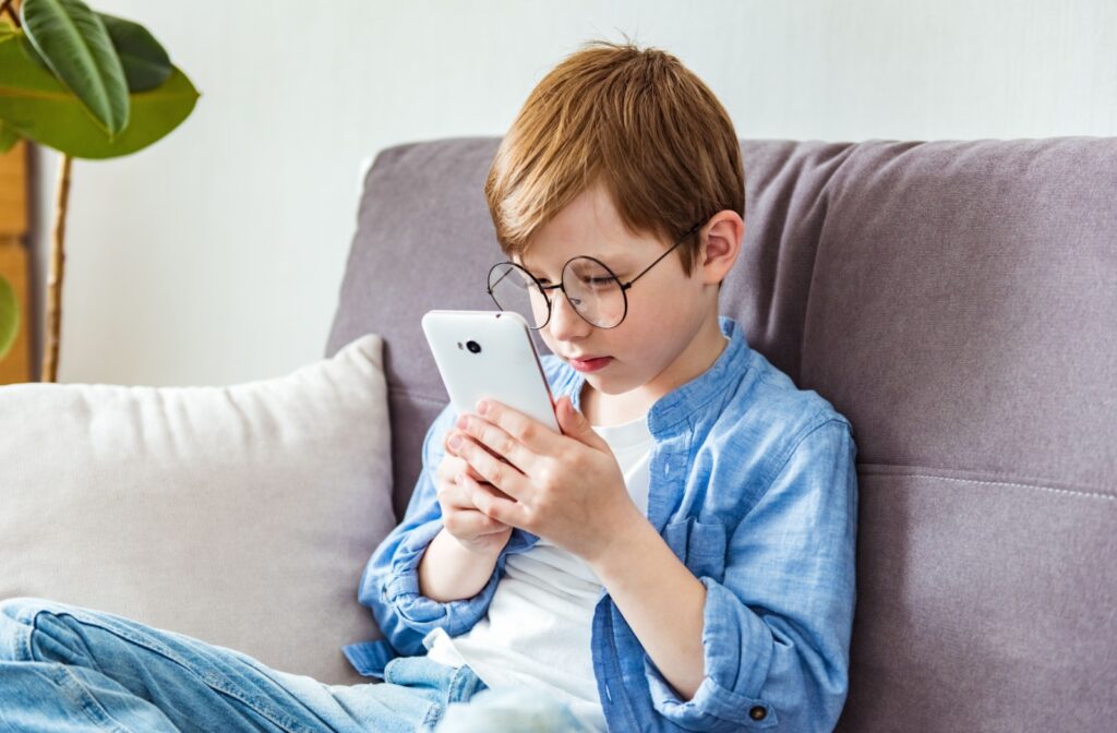 Young boy with large glasses looking closely at mobile phone.
