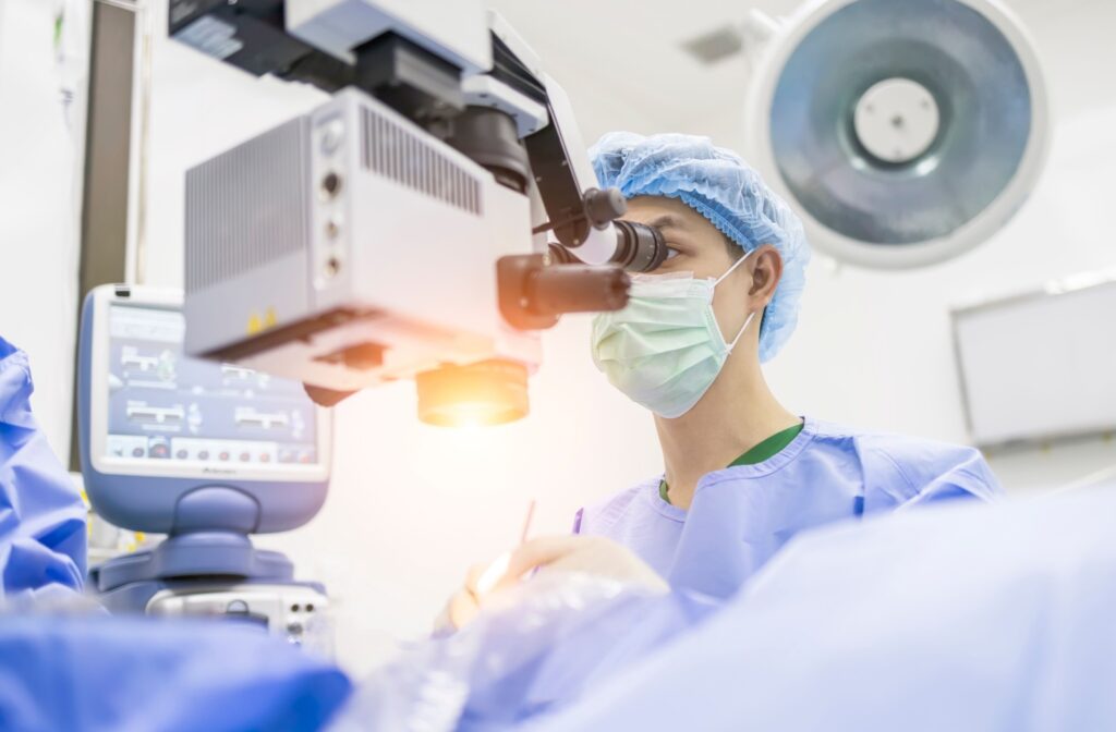 A surgeon wearing a surgical gown, performs cataract surgery using a microscope in a brightly lit operating room.