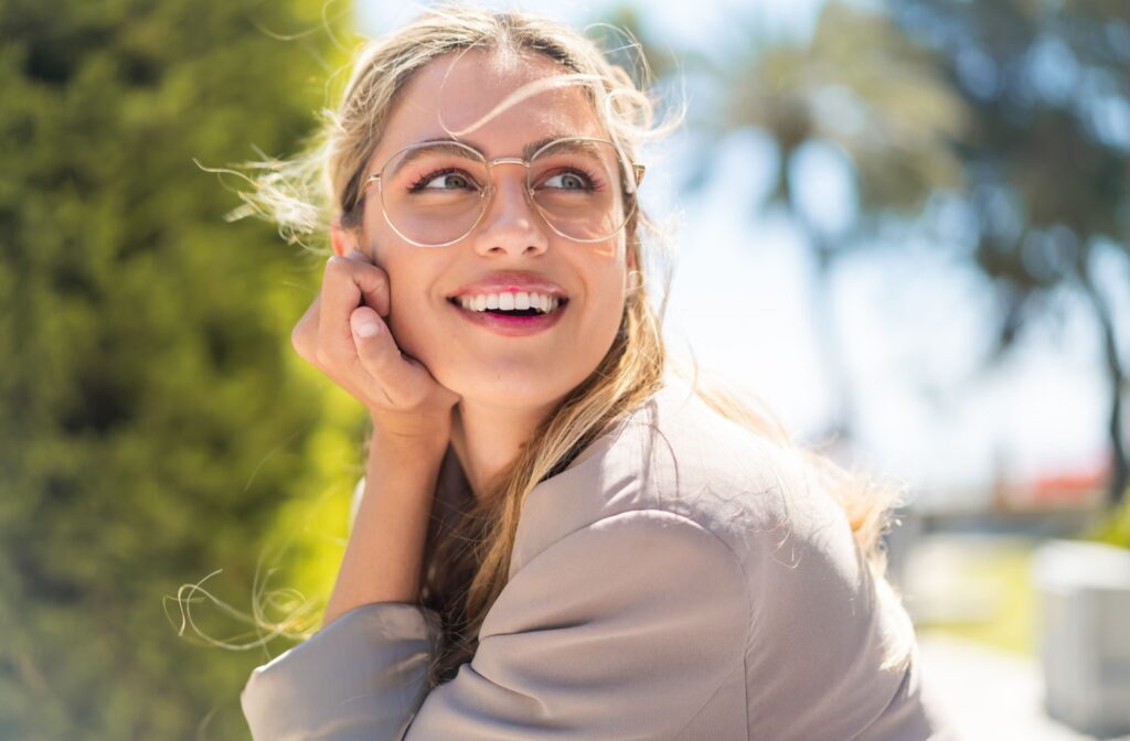A woman outside, smiling, wearing a pair of comfortable eyeglasses suited for all day wear.